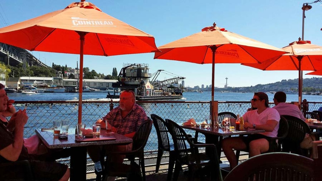 Watching the barges float by, outside deck, Ivars Salmon House, orange umbrellas for protection from the sun, Portage bay, Seattle, Washington, USA